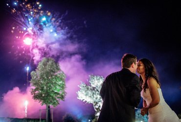 Couple sharing a kiss as colorful fireworks light up the night sky behind them