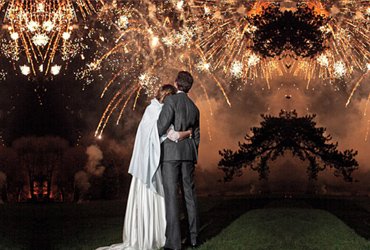 Groom and bride embracing beneath a golden burst of wedding fireworks at night