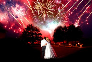 Bride and groom kissing beneath red and gold fireworks at their beach wedding celebration