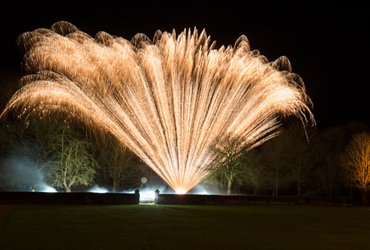 Wide golden fan of fireworks filling the night sky during a beach celebration